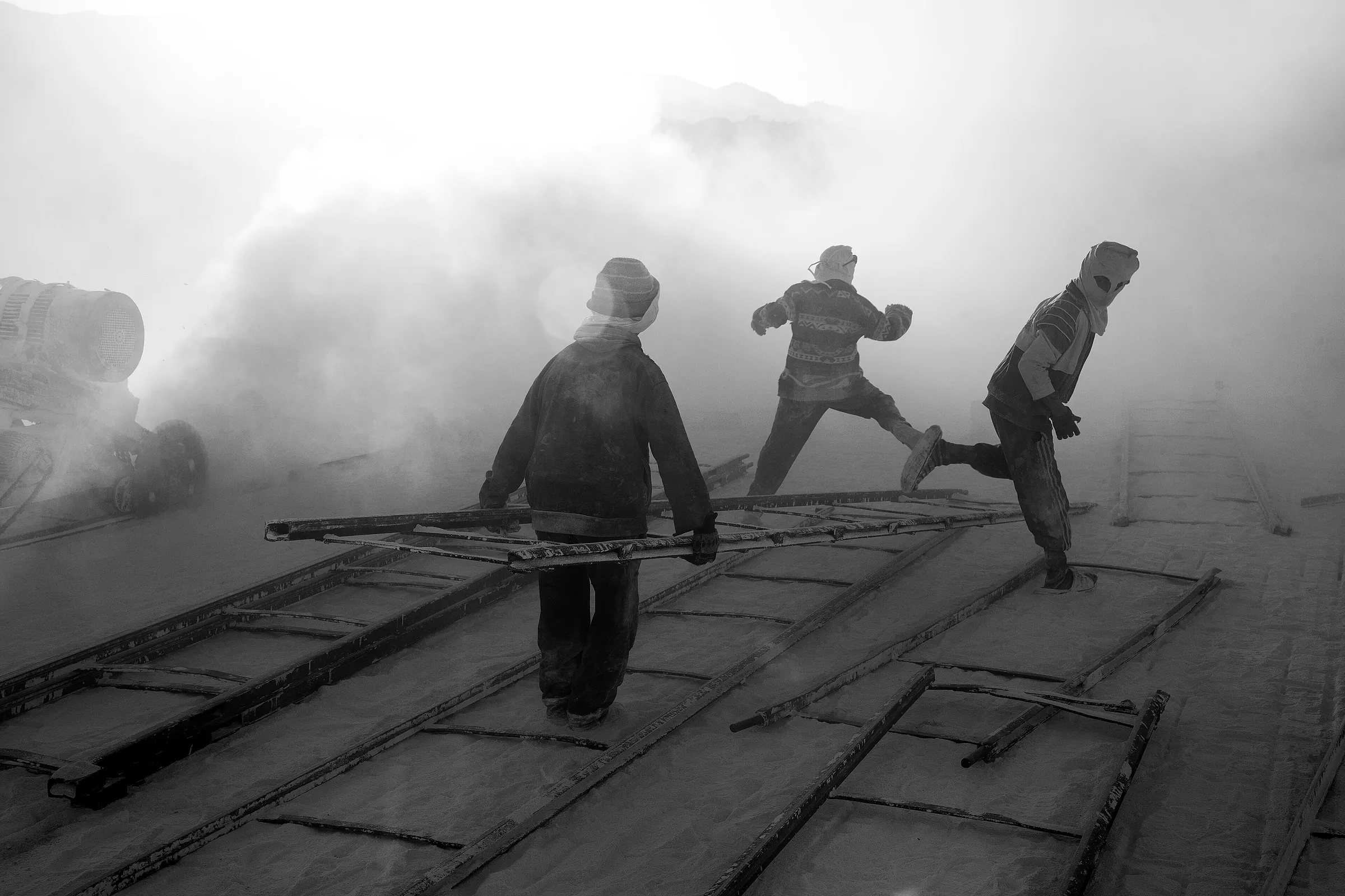 Three workers on a screen deck in heavy dust at a limestone quarry.